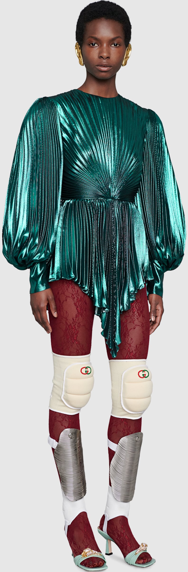 A model wearing Kneepad with embroideries, Metal left ear accessory, Metal right ear accessory, Iridescent lamé pleated mini dress, Floral lace tights, Mid-heel slide with tiger head